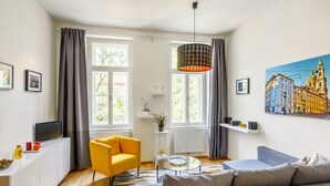 A modern living room with a sofa, a yellow armchair, a glass coffee table, and a painting of a cityscape. - Beautiful Apartment with Private Terrace in Central Prague (Praha 3)