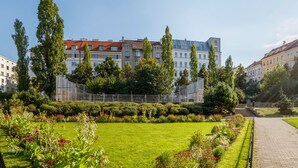 A well-maintained garden with a paved walkway, surrounded by buildings with red-tiled roofs and a variety of trees.