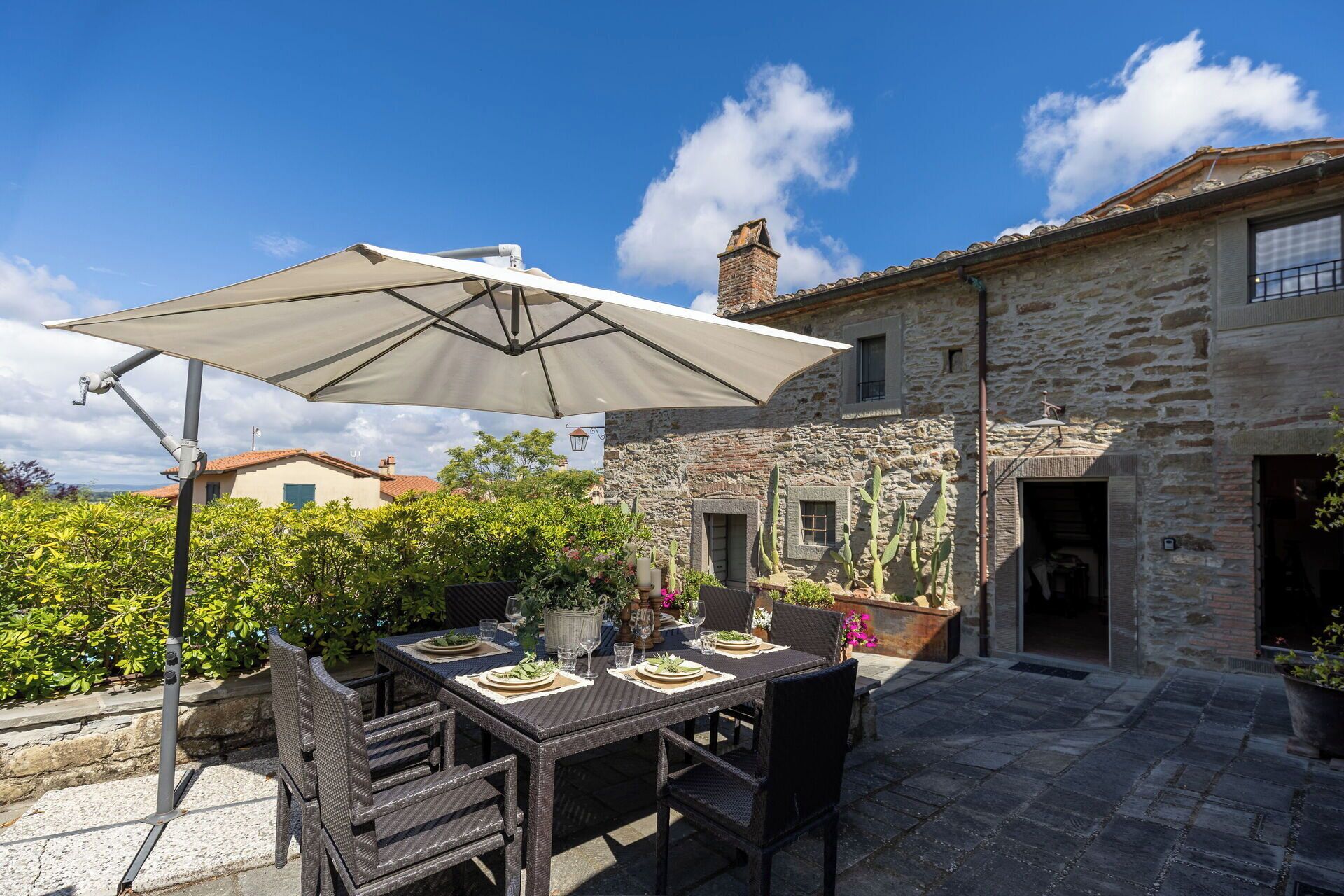Une terrasse extérieure avec une table dressée pour le repas, un grand parasol et un bâtiment en pierre en arrière-plan.