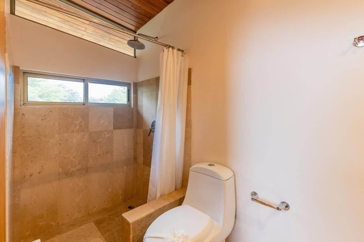 A bathroom with a shower, toilet, and a window.
