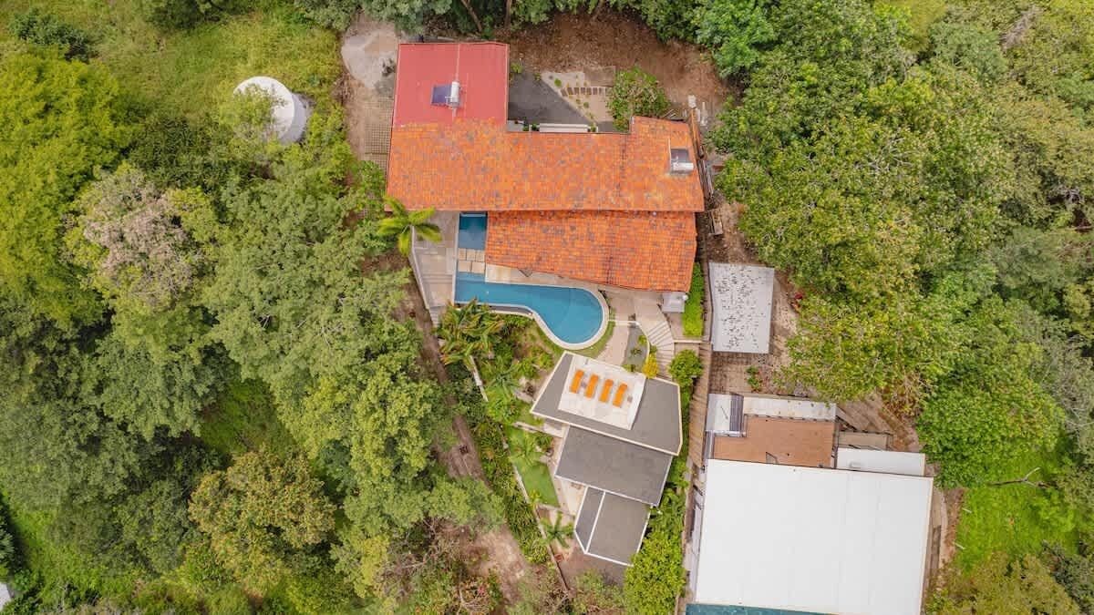 An aerial view of a house with a swimming pool, surrounded by dense greenery.