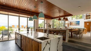 A modern kitchen with a large island, wooden cabinets, and pendant lighting.