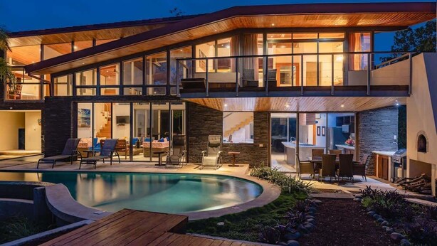 A modern two-story house with a swimming pool, outdoor seating, and a stone facade.