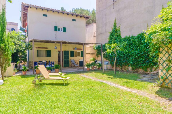 A two-story building with a covered patio area, a lounge chair, and potted plants.