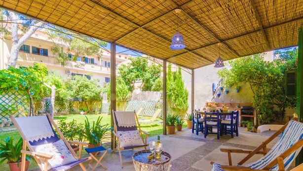 A covered outdoor seating area with lounge chairs and a table, surrounded by potted plants and a view of buildings in the background. - PENYA - Chalet with private garden in S'Illot. Free WiFi (Manacor)