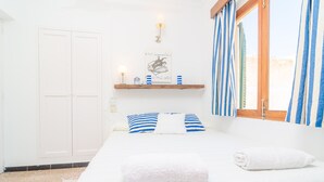 A neatly made bed with white and blue striped pillows, a white towel, and a framed picture on the wall. - PENYA - Chalet with private garden in S'Illot. Free WiFi (Manacor)
