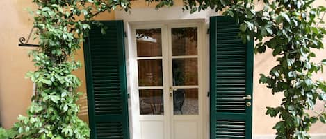 A door with green shutters, a small table, and chairs outside a building with a yellow wall.