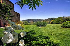 Stroll through the serene garden, surrounded by lush greenery and vibrant flowers, including white roses, beneath the historic stone building's arched entrance.