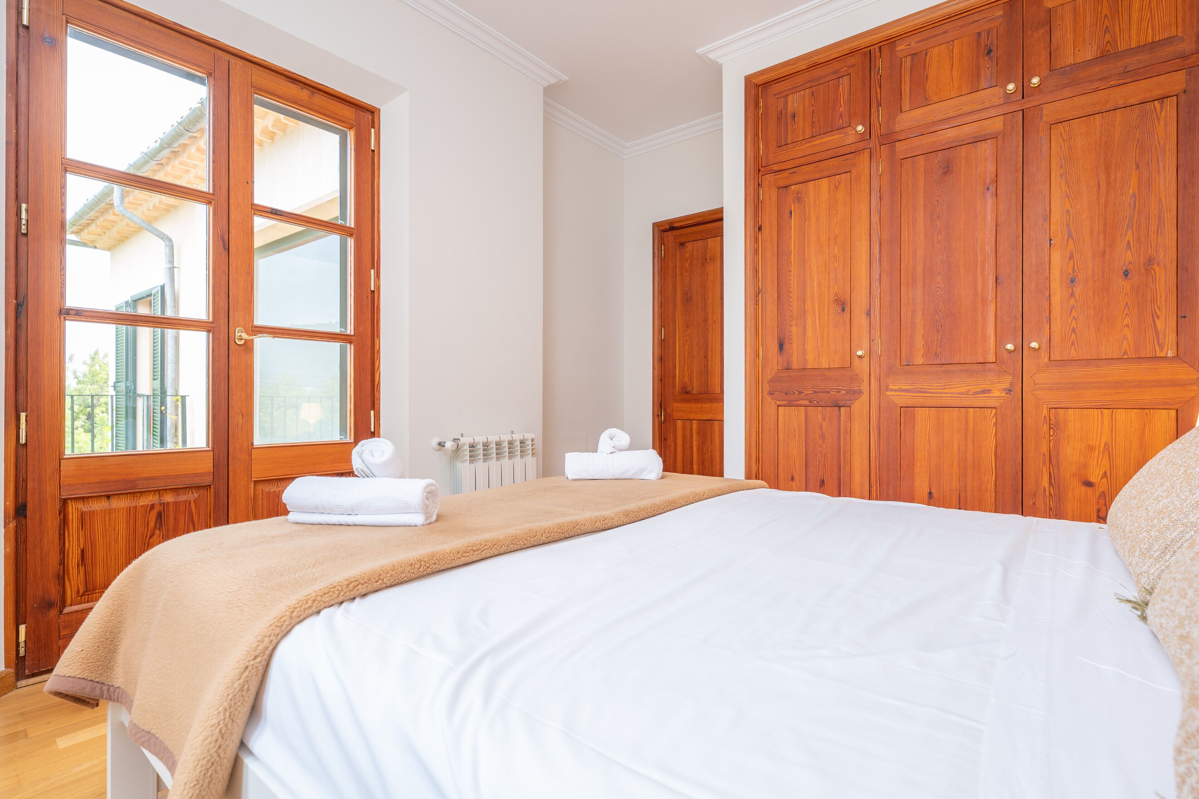 Ein Schlafzimmer mit einem großen Bett, einem Holzschrank und einem Fenster mit Blick auf ein Gebäude.