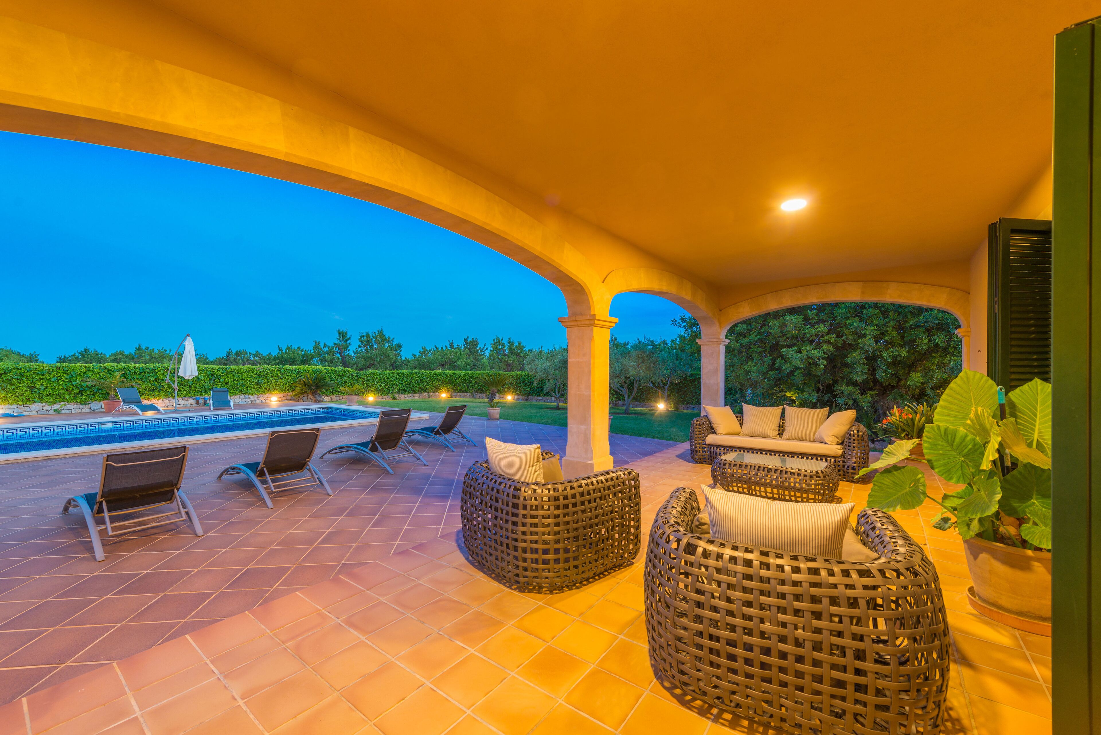 A covered outdoor seating area with wicker furniture and a pool in the background.