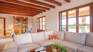 Un soggiorno con divano beige, travi in legno a soffitto, zona pranzo con sedie e tavolo e ampie finestre con vista.