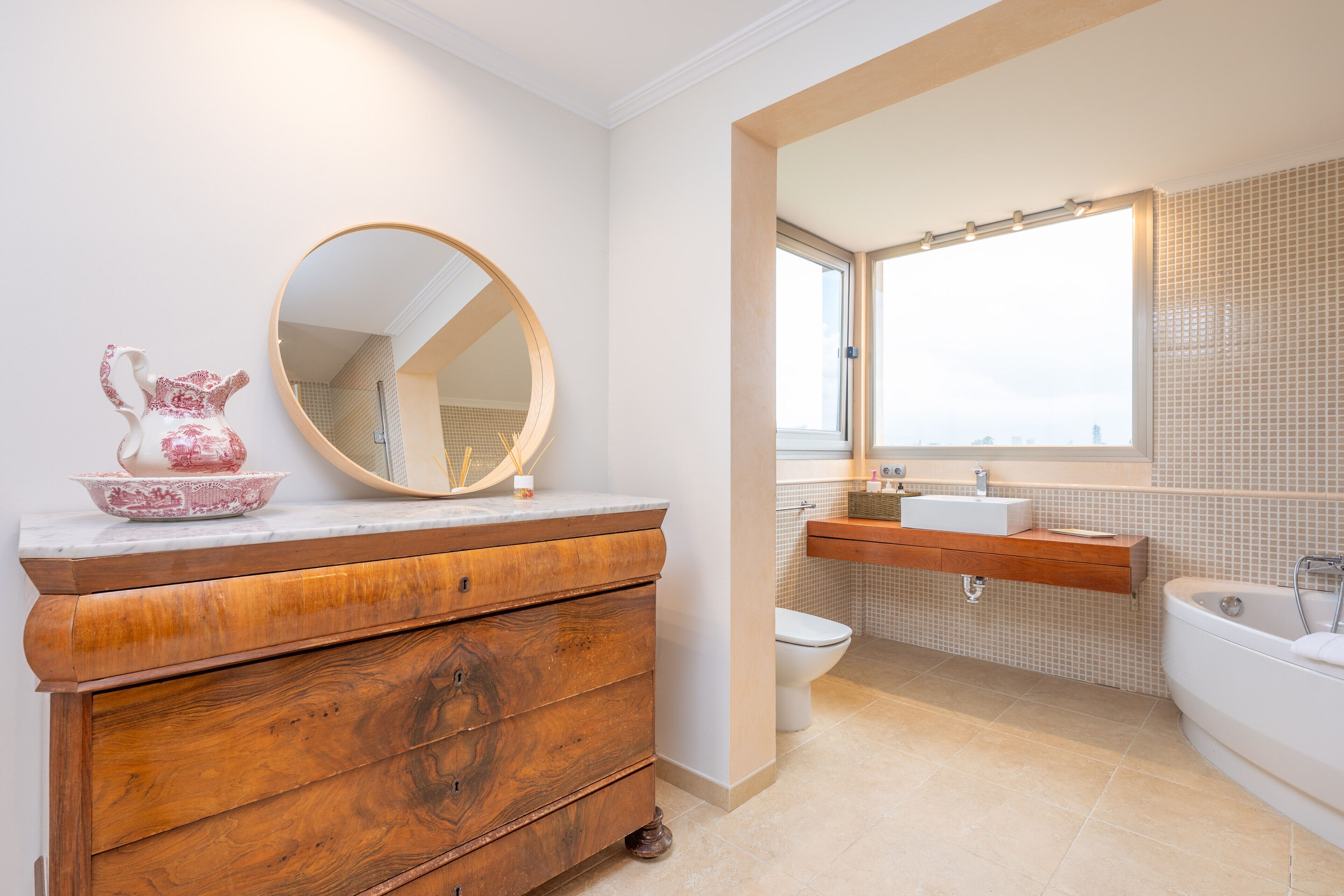 A bathroom with a wooden vanity, a round mirror, a white sink, and a bathtub.