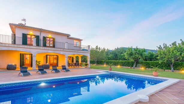 Vista di una piscina con una villa, area relax esterna e un giardino curato.
