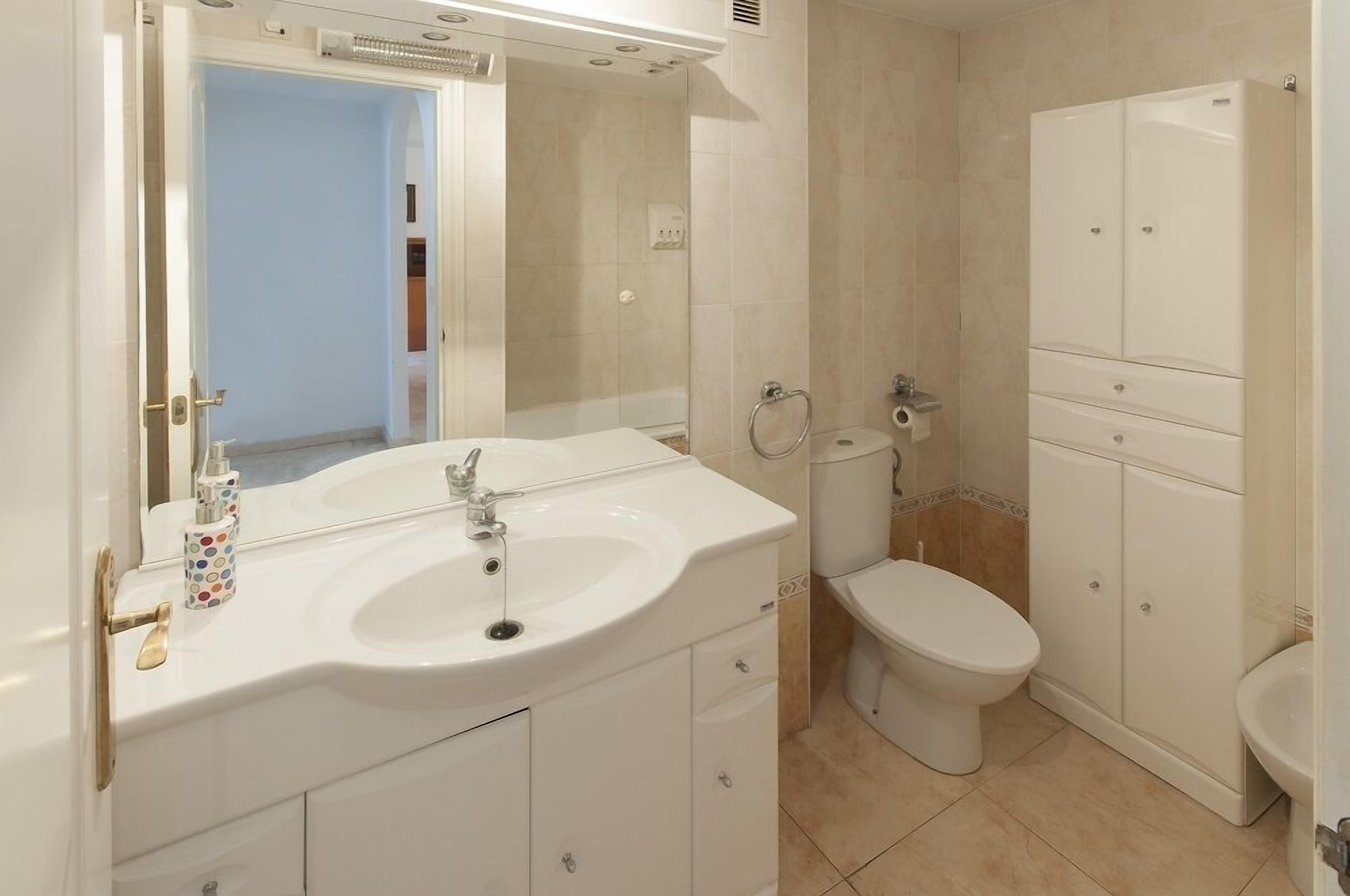 A bathroom with a white sink, toilet, and shower. There is a mirror above the sink and a cabinet to the right.