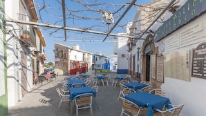 An outdoor café with tables and chairs, surrounded by buildings with signs and a menu board. - CASCADES - Apartment with shared pool in Dénia. (Denia)
