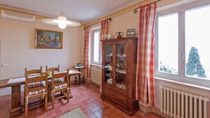 Un comedor con mesa y sillas de madera, un armario con puertas de cristal y una ventana con cortinas.