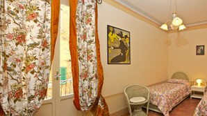 Un dormitorio con dos camas, una silla, un cuadro en la pared y una ventana con cortinas.