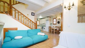 A living room with a blue sofa and a white sofa, a wooden staircase, and a kitchen in the background.