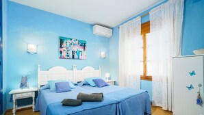 A room with two beds, a white wardrobe, a painting on the wall, and a window with curtains.