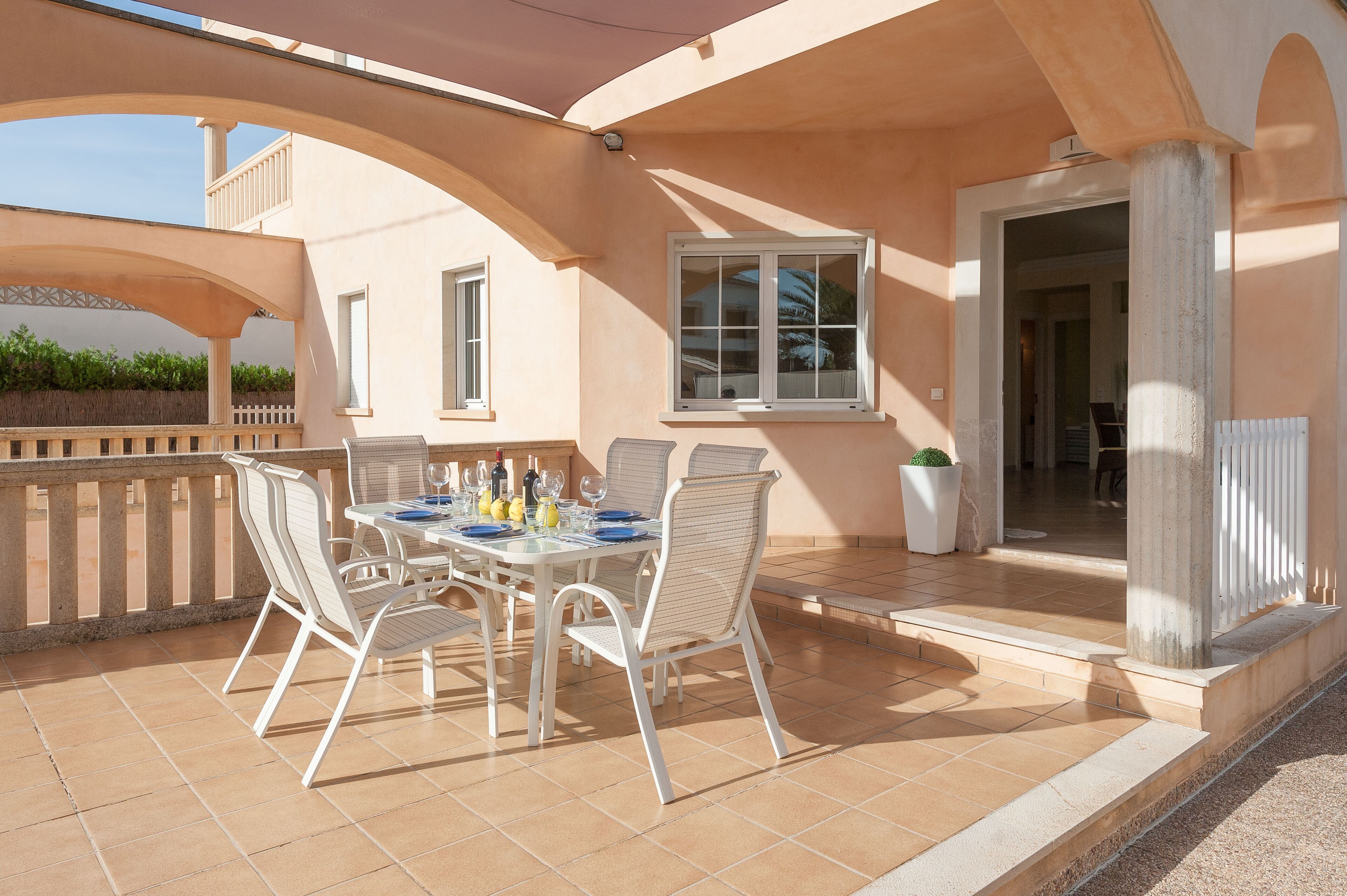 A covered outdoor dining area with a table set for four, surrounded by white chairs, and a potted plant to the side.