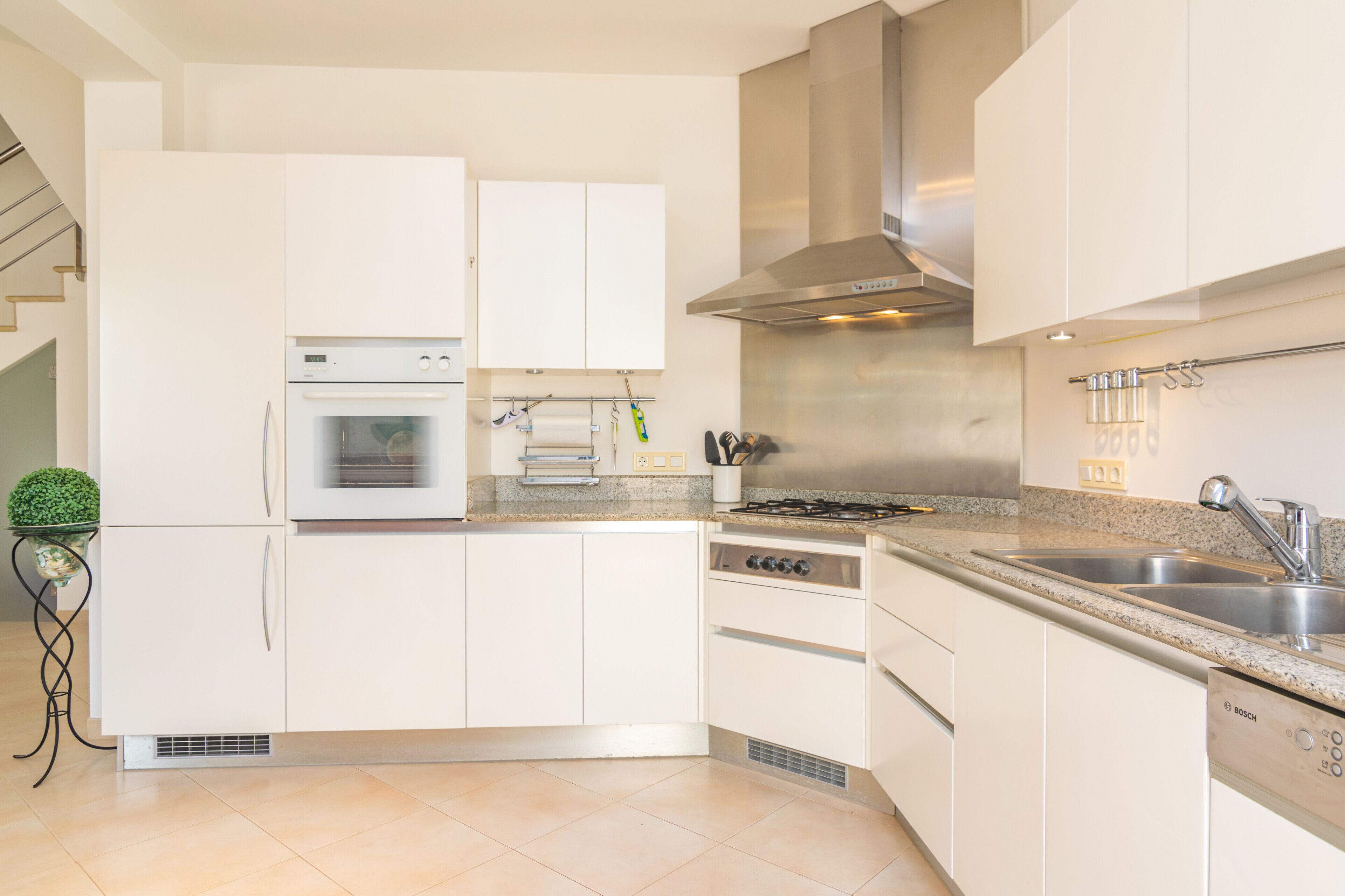 Une cuisine moderne avec des meubles blancs, un four encastré, une cuisinière et un lave-vaisselle Bosch.