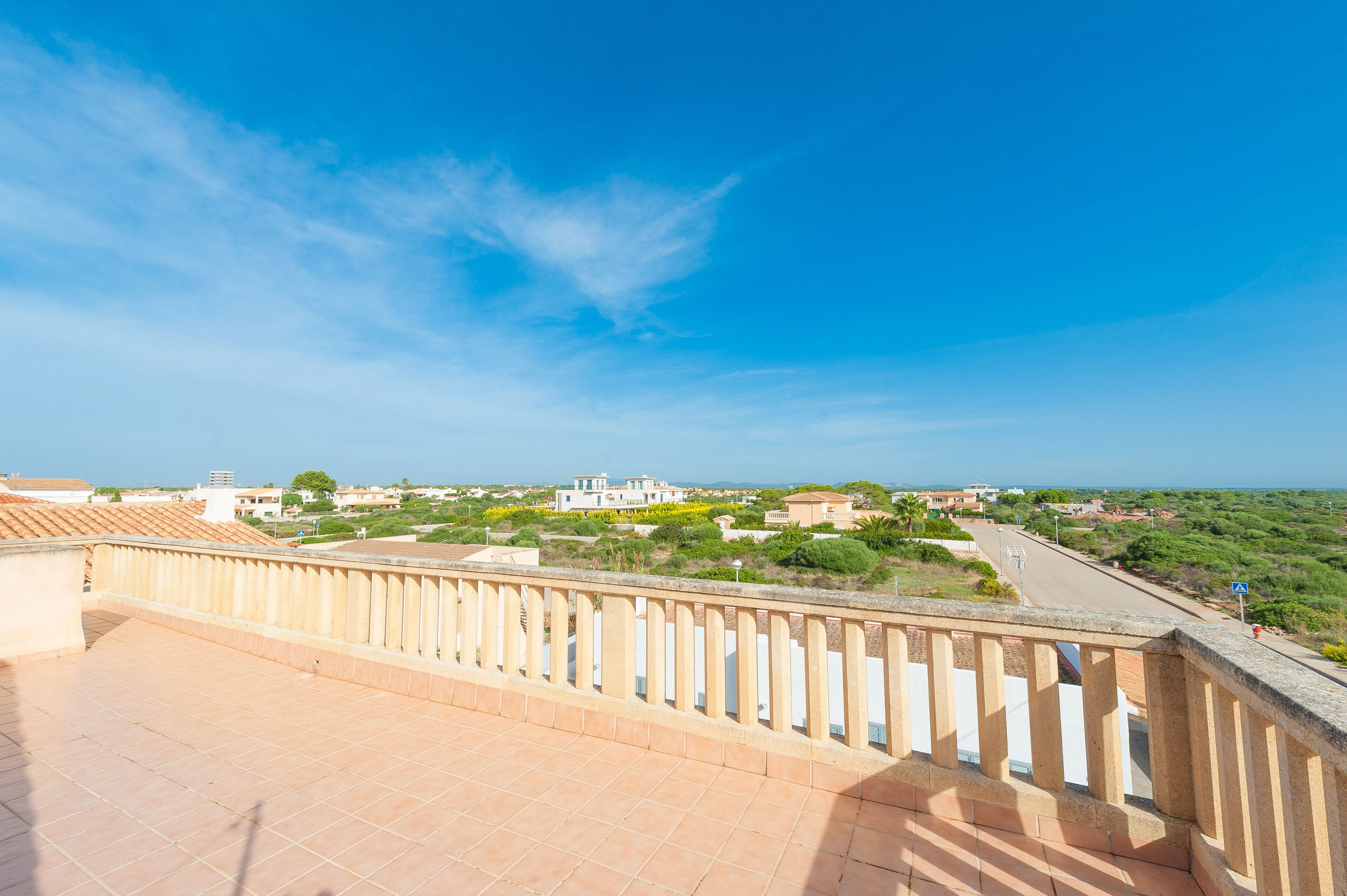 A terrace with a tiled floor and a balustrade overlooking a coastal landscape with buildings and greenery.