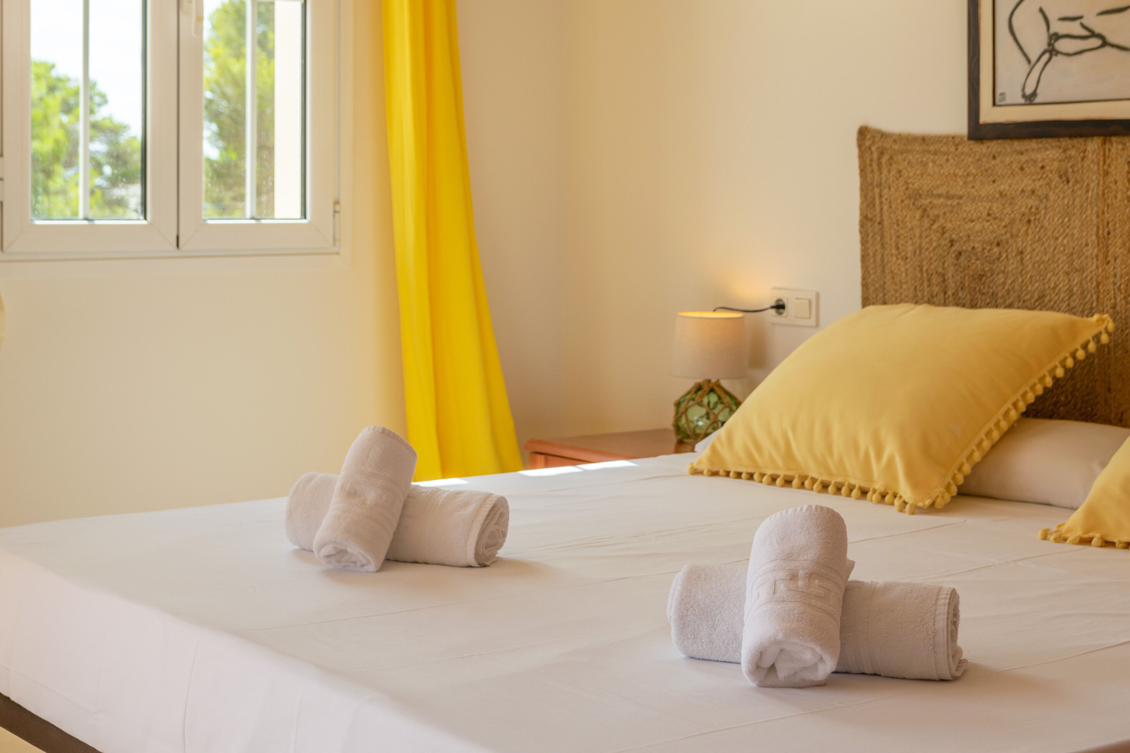 A neatly made bed with two towels, a yellow curtain, and a lamp on a bedside table.