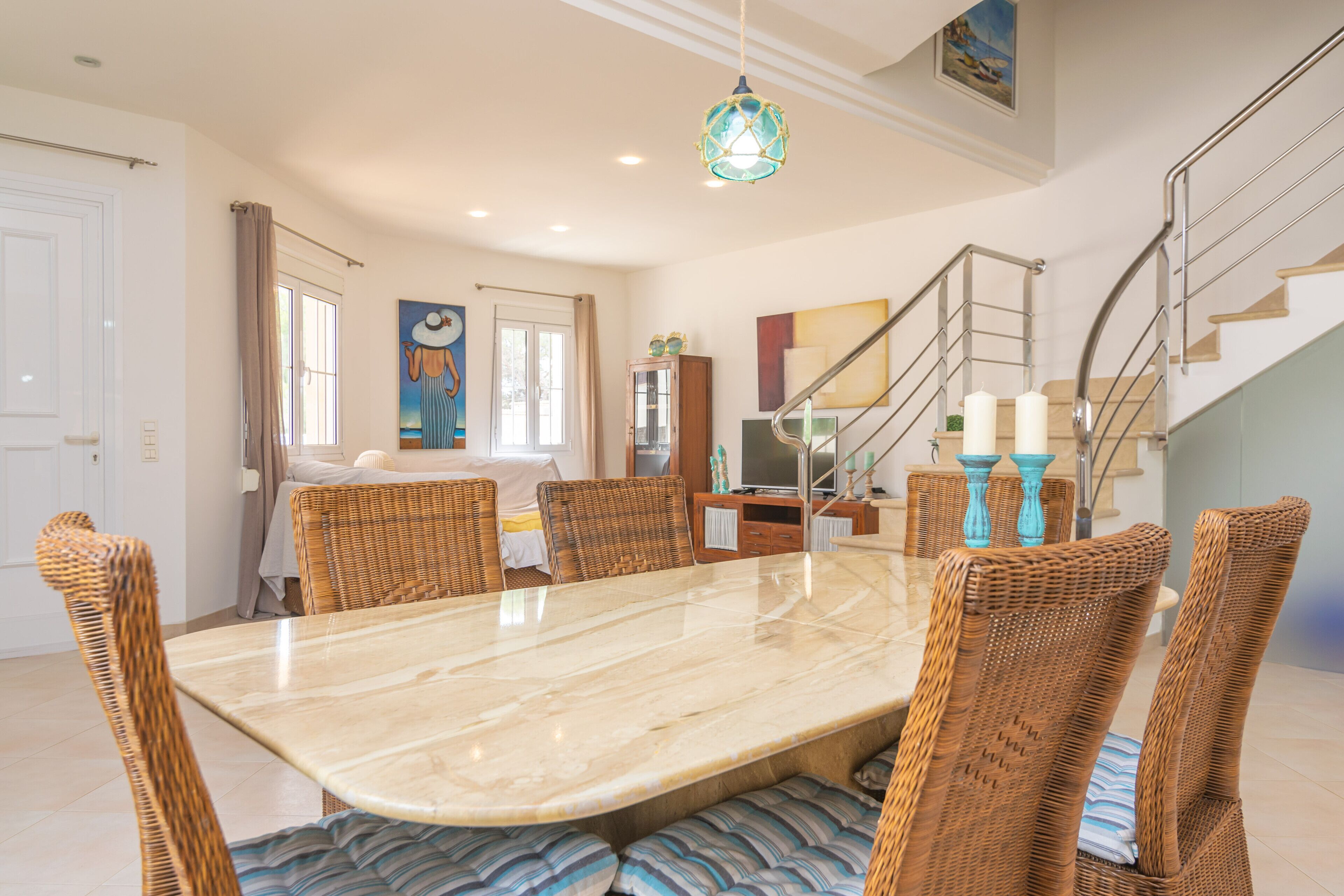 Un coin repas avec une table en marbre, des chaises en osier et un escalier doté de rampes en métal.