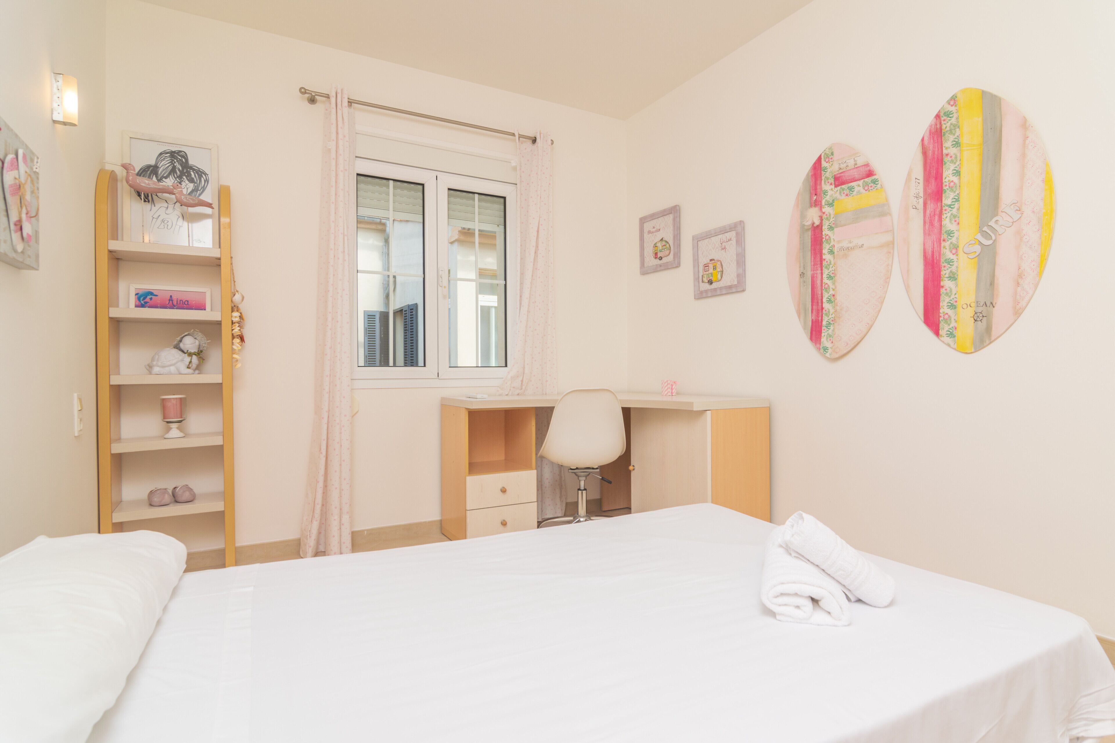 A bedroom with a bed, a desk, and a chair. There are shelves with items on them.