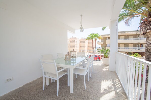 A balcony with a glass table and chairs, a hanging light fixture, and a view of buildings and palm trees.