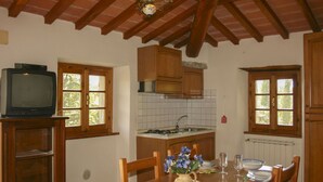 A kitchen with wooden cabinets, a tiled backsplash, a dining table with chairs, a vase with flowers, and a television on a stand. - Cosy apartment for 2 guests with WIFI, pool, TV and pets allowed, close to Cortona (Castiglion Fiorentino)