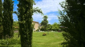 A grassy courtyard with a stone building in the background, surrounded by trees. - Cosy apartment for 2 guests with WIFI, pool, TV and pets allowed, close to Cortona (Castiglion Fiorentino)