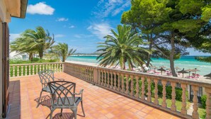 A terrace with a view of the sea, palm trees, and outdoor seating.