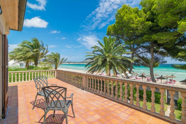 A terrace with a view of the sea, palm trees, and outdoor seating.