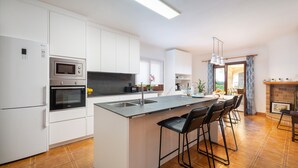 A modern kitchen with white cabinetry, a central island with bar stools, a built-in oven, and a large window.