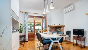 A modern dining area with a white table, blue chairs, and a television on a wooden stand.