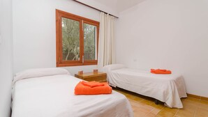 A bedroom with two beds, a window with curtains, a wooden nightstand, and a tiled floor. - ES JAÇ - Villa with terrace in Cala s'Almonia with free Wi-Fi (Cala Llombards)