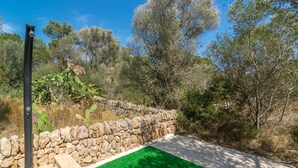 A stone wall with a green artificial turf area, surrounded by trees and vegetation. - ES JAÇ - Villa with terrace in Cala s'Almonia with free Wi-Fi (Cala Llombards)
