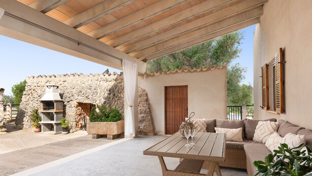 An outdoor patio with a wooden table and wicker sofa, stone walls, and potted plants. - SON ROSSINYOL  - Beautiful country house with above ground pool in rural and quiet area. F (Llubí)