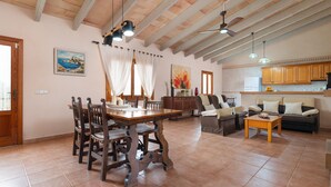 A spacious living area with a wooden dining table, chairs, a sofa, and a coffee table. There is a kitchen area with wooden cabinets and a refrigerator. - SON ROSSINYOL  - Beautiful country house with above ground pool in rural and quiet area. F (Llubí)