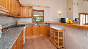 A kitchen with wooden cabinets, a granite countertop, a window, and a small wooden stool. - SON ROSSINYOL  - Beautiful country house with above ground pool in rural and quiet area. F (Llubí)