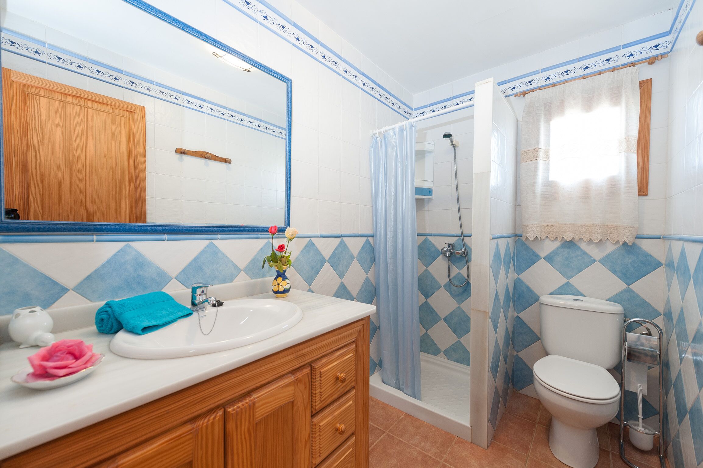 A bathroom with a white sink, wooden vanity, a mirror, a shower, and a toilet.