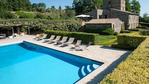 Una piscina con sillas de descanso, un edificio de piedra y jardines cuidados.