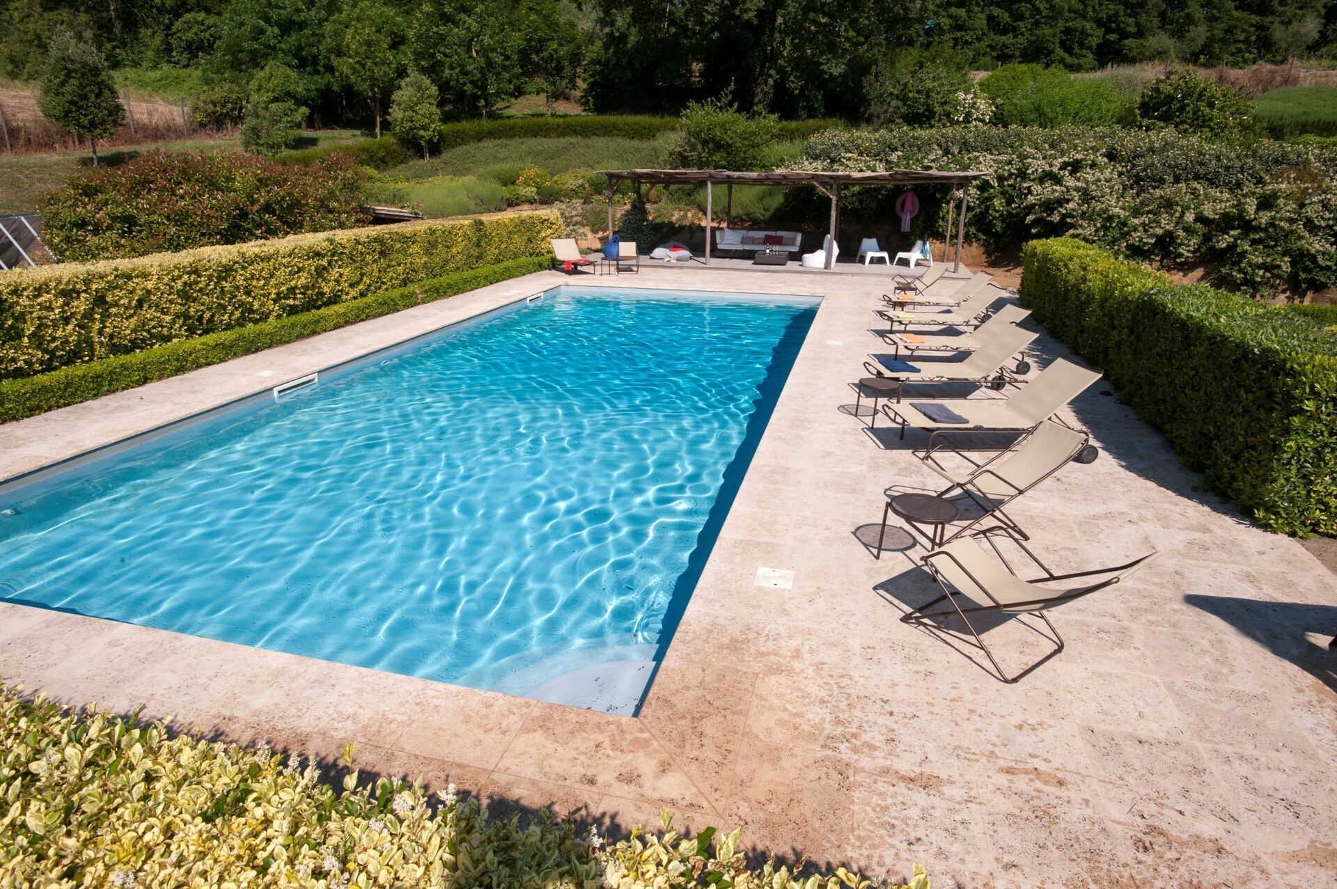 Une piscine rectangulaire à l’eau d’un bleu limpide, entourée d’une terrasse carrelée. Des chaises longues sont alignées le long du bord de la piscine.