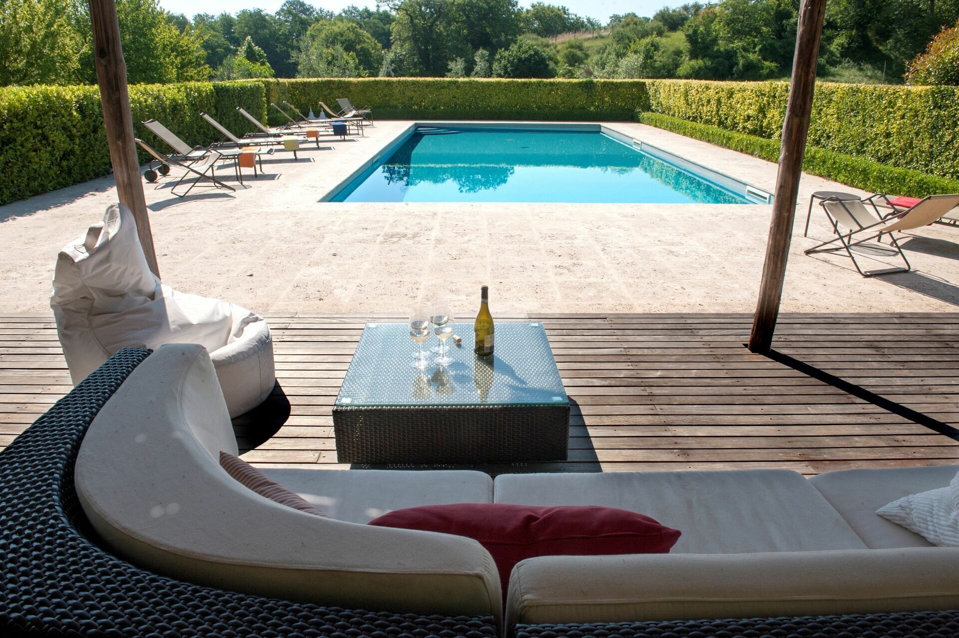 Un espace aménagé au bord de la piscine, avec des chaises longues, une table sur laquelle se trouvent une bouteille et des verres, et une vue sur la piscine.