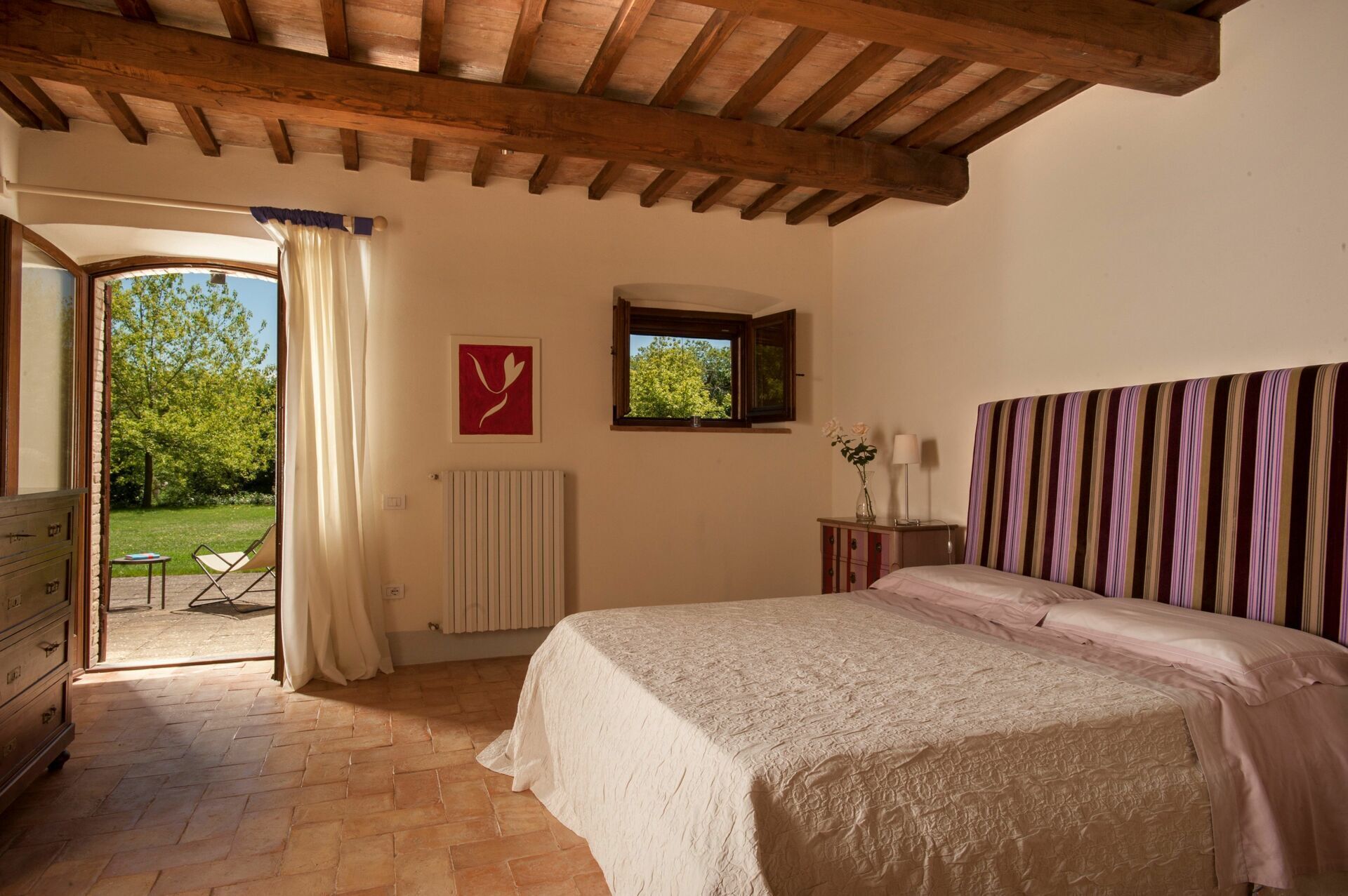 A bedroom with a bed, a radiator, a window, and a view of the outdoors.