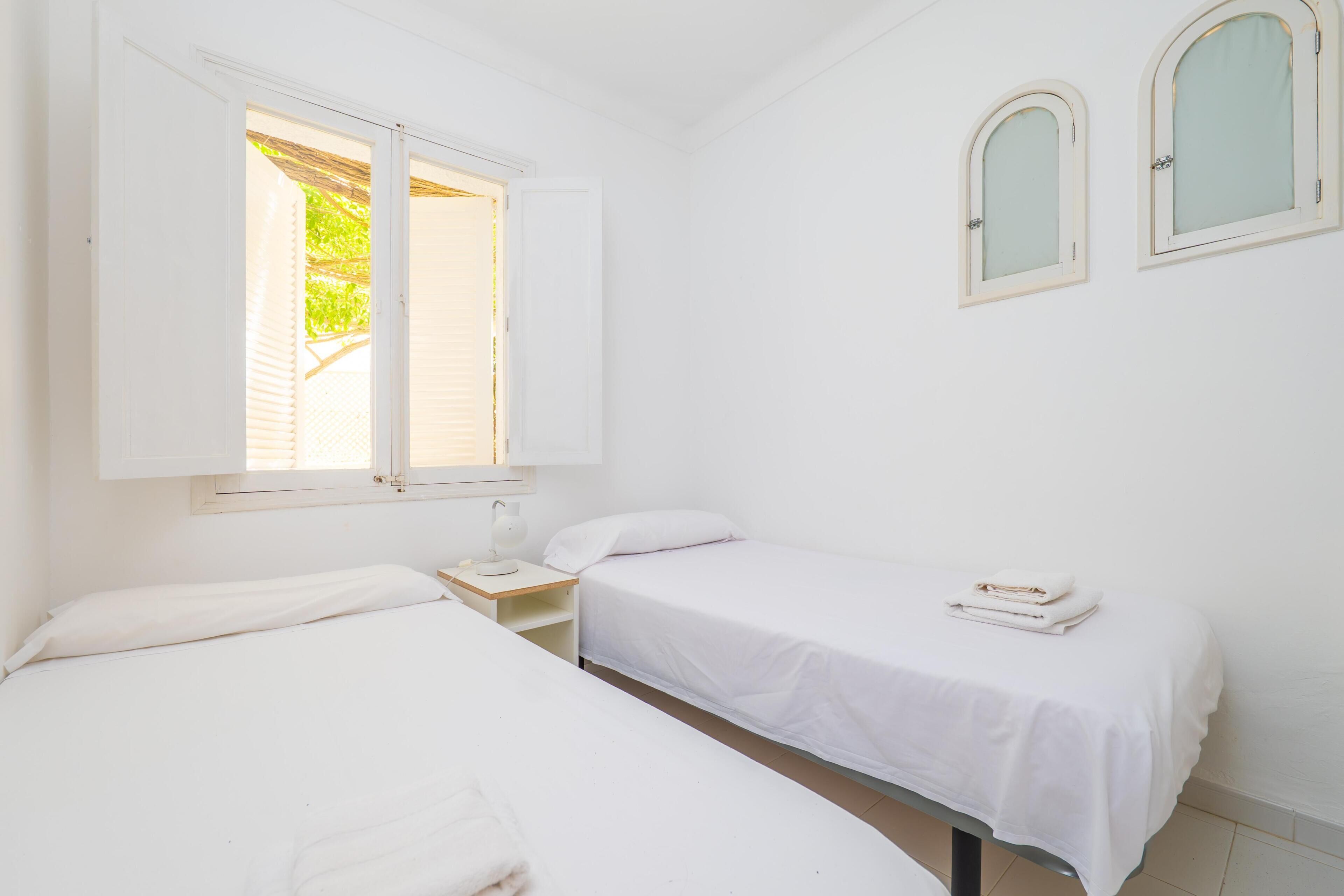 A room with two beds, a window, and a small table with a lamp.
