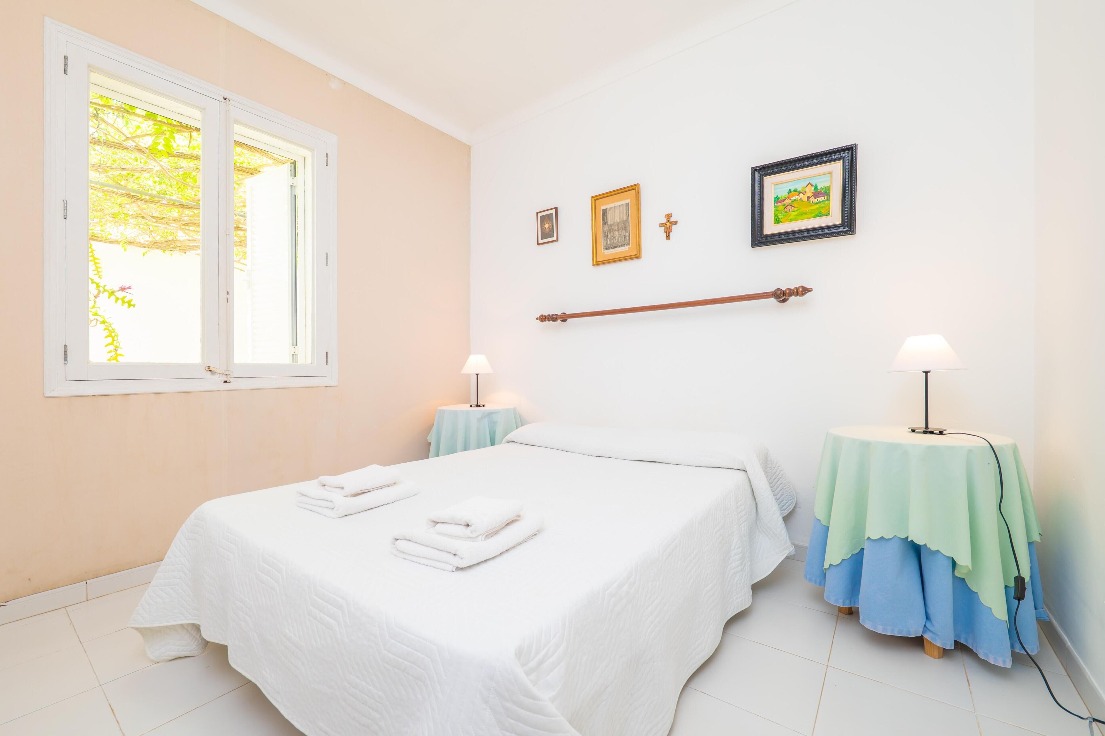 A bedroom with a bed, two bedside tables, a window, and wall-mounted pictures.