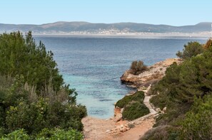 A coastal landscape with a clear view of the sea, rocky terrain, and a path leading to the water.