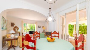 A dining area with a round table, red chairs, a fruit bowl, and a view of greenery outside. - CAN FERRO - Villa with private pool in Cala Blava. Free WiFi (Llucmajor)